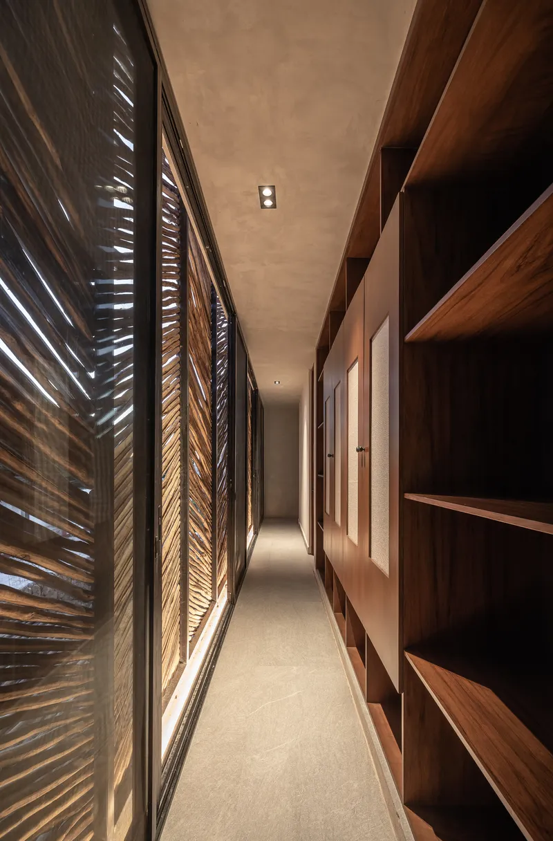 Narrow corridor with slatted timber screen on one side and built-in shelving opposite under warm downlighting