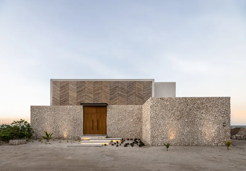 Front entrance with gabion stone walls and herringbone timber panel above a wooden door at twilight