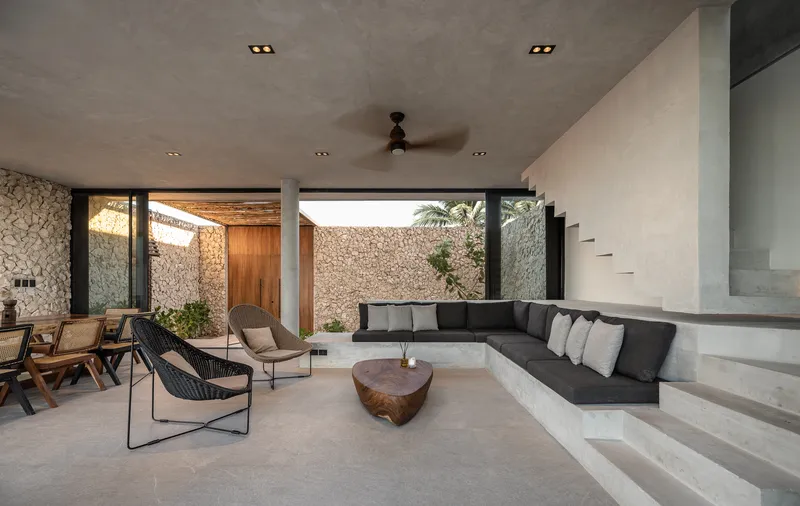 Sunken living room with built-in concrete seating opening to a courtyard with stone walls and palms