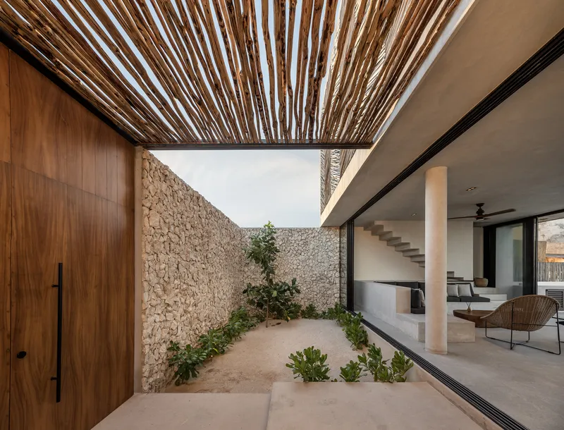 Covered courtyard with timber slat canopy connecting stone walls and glazed living spaces with planted bed