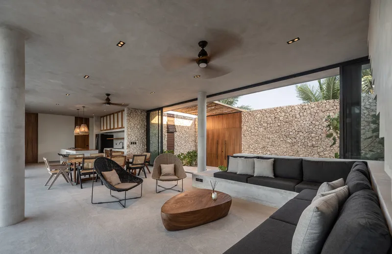 Open-plan living space with concrete ceiling and large opening framing a courtyard with stone wall