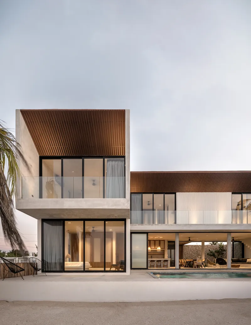 Two-story facade with white concrete volumes and ribbed timber soffits at twilight