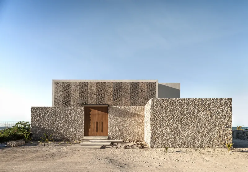 Street view of the facade featuring herringbone timber screens above textured stone walls and a central timber door