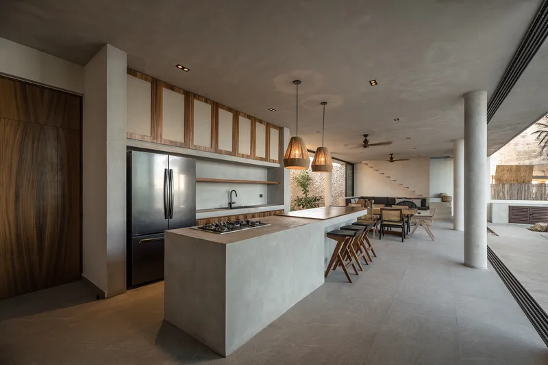 Open kitchen and living area with concrete island, woven pendant lights, and clerestory windows above timber-framed glazing