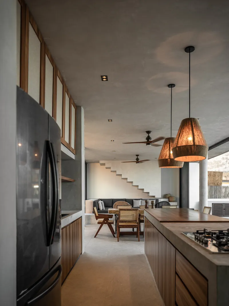View through the kitchen toward floating concrete stairs and living area with woven pendant lights overhead