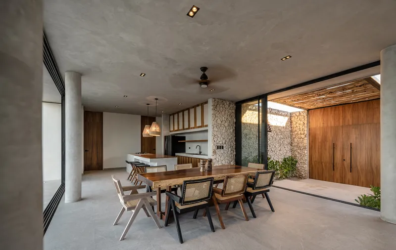 Dining area looking toward stone courtyard wall and timber screen with woven pendant lights suspended from concrete ceiling