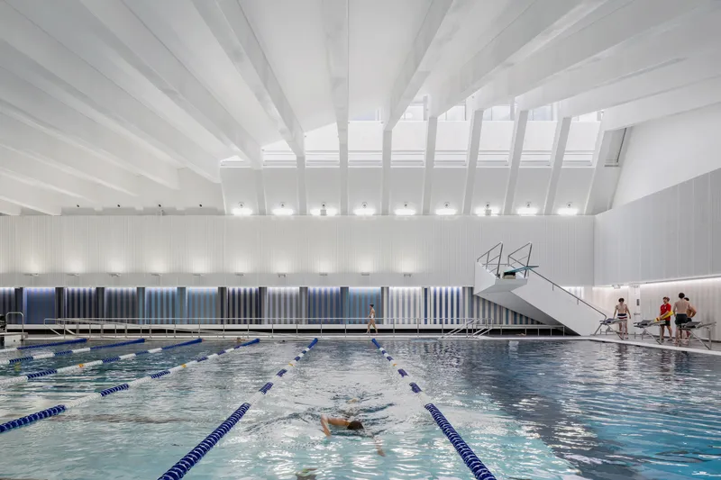Indoor lap pool with diving platform under white beam ceiling and vertical ribbed wall panels