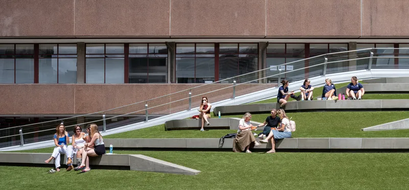 Tiered outdoor seating with alternating grass and concrete steps occupied by students in sunshine