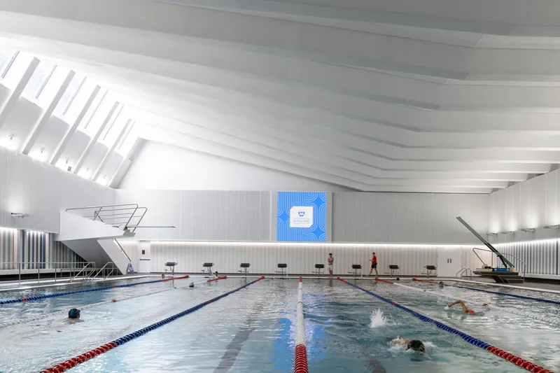 Indoor lap pool with white ribbed ceiling and swimmers in lanes under overhead skylights