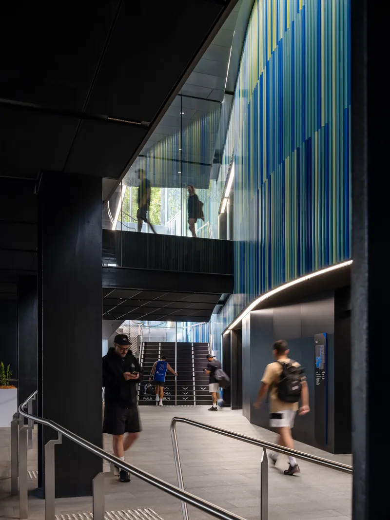 Interior atrium with suspended walkway and multicolored vertical screens above visitors in motion