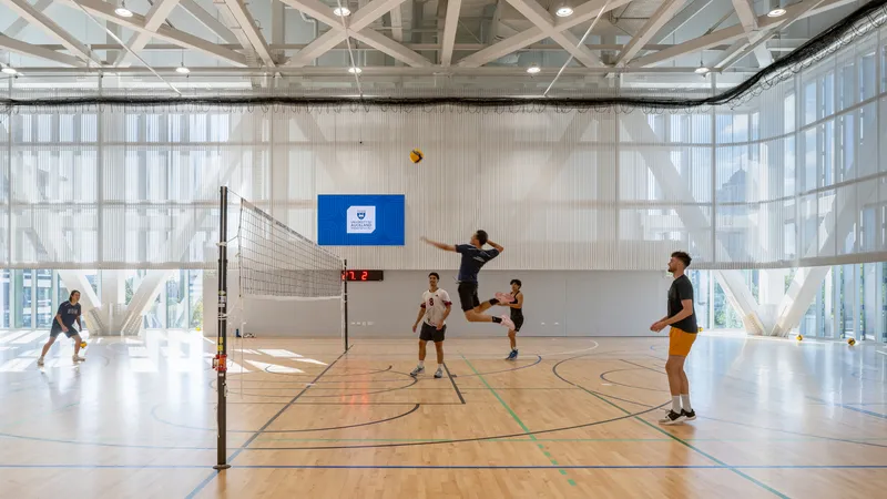 Indoor volleyball court with exposed white trusses and translucent curtain walls during afternoon play