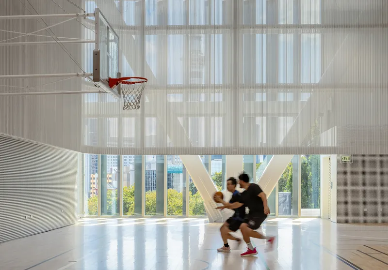 Interior basketball court with suspended hoop and two players in motion beneath translucent ceiling panels
