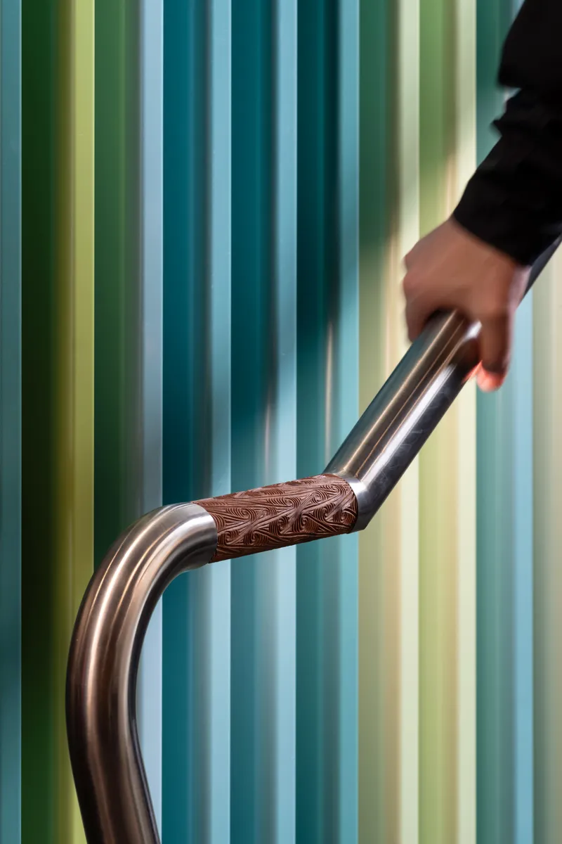Hand gripping curved metal handrail with patterned grip against gradient blue and green wall panels