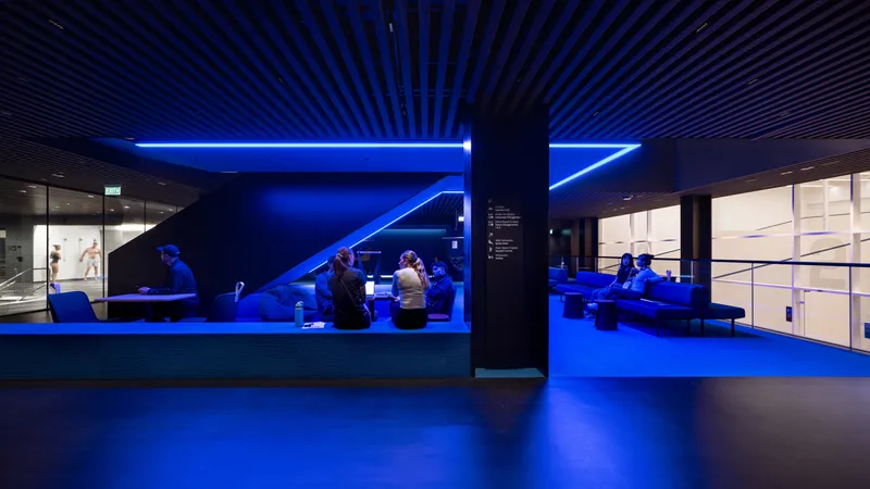 Interior lounge space illuminated by blue linear lighting with visitors seated beneath angular ceiling slats