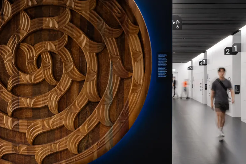 Carved wooden circular medallion beside corridor with numbered wayfinding and visitor passing through at speed