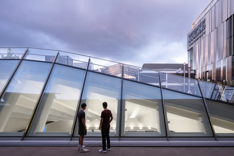 Sloped glass wall with black steel frames reflecting two figures at twilight