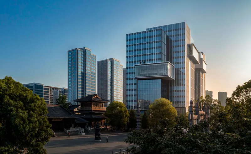 Cluster of glass tower blocks rising beyond a traditional temple structure and surrounding trees