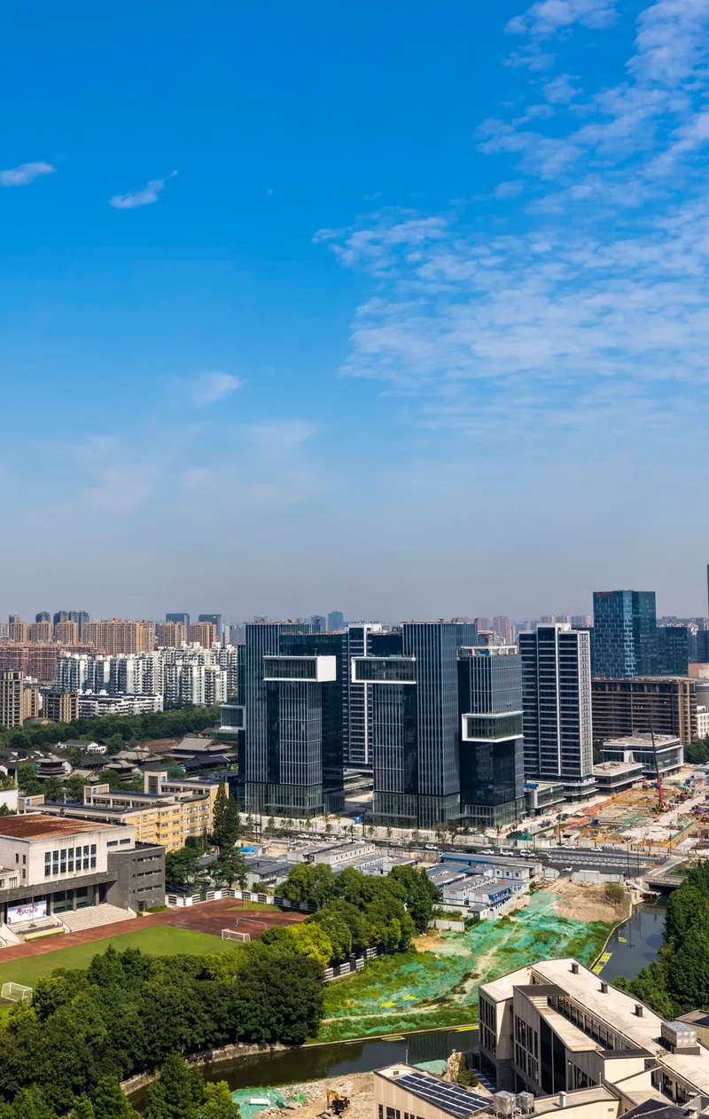 Aerial view of offset glass office towers amid low-rise buildings and a green canal corridor