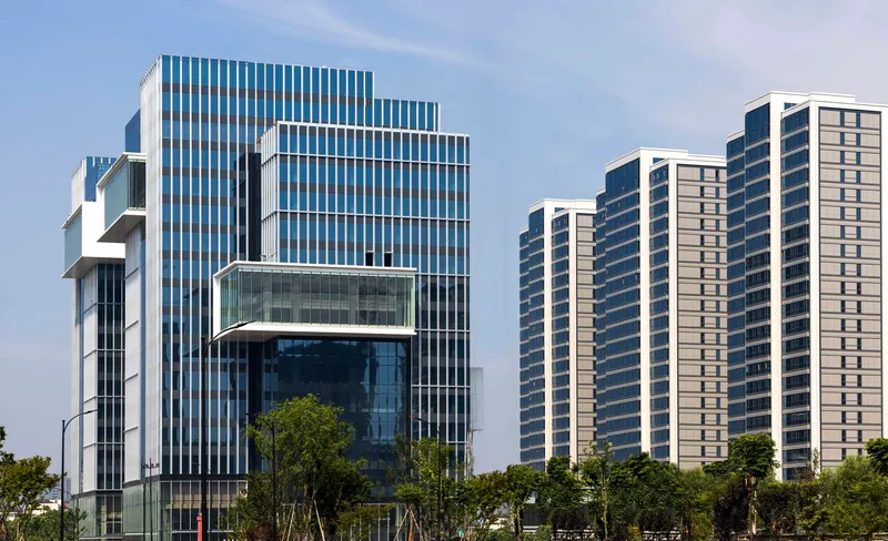 Vertical louvered glass facade with cantilevered volumes beside rows of residential high-rises
