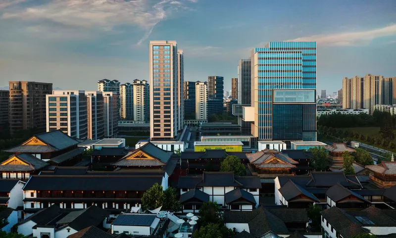 Cluster of stepped glass and concrete towers behind the low-rise traditional timber rooflines at sunset
