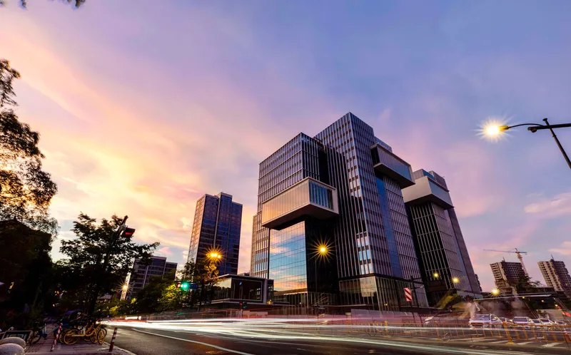 Articulated facade of cantilevered glass and metal volumes above a busy street at dusk