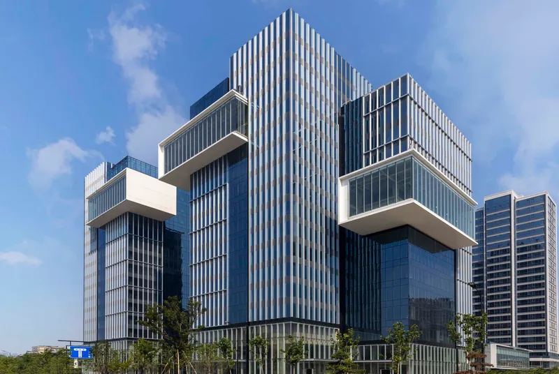 Central tower with vertical ribbed cladding flanked by cantilevered glass volumes under blue sky