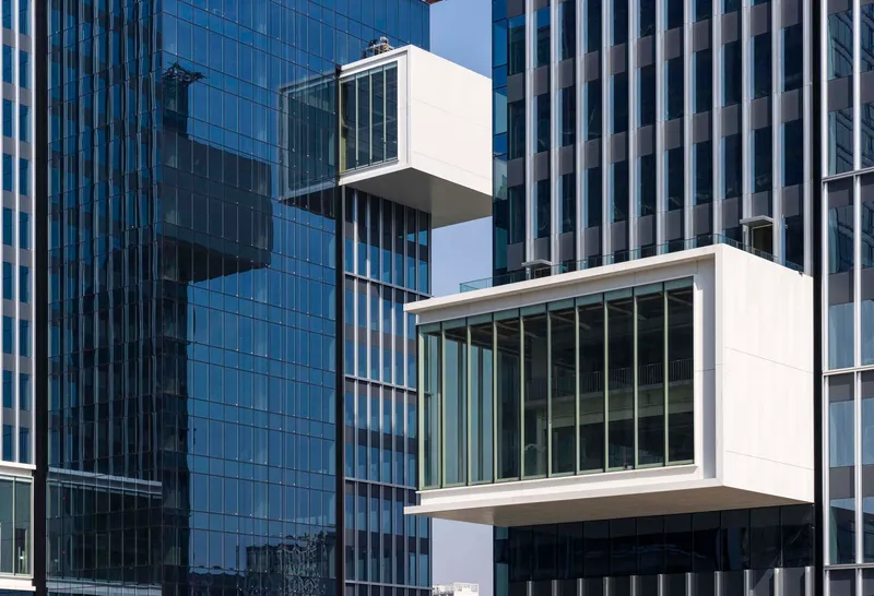 Two stacked white cantilevered glass boxes projecting from a blue glass curtain wall tower