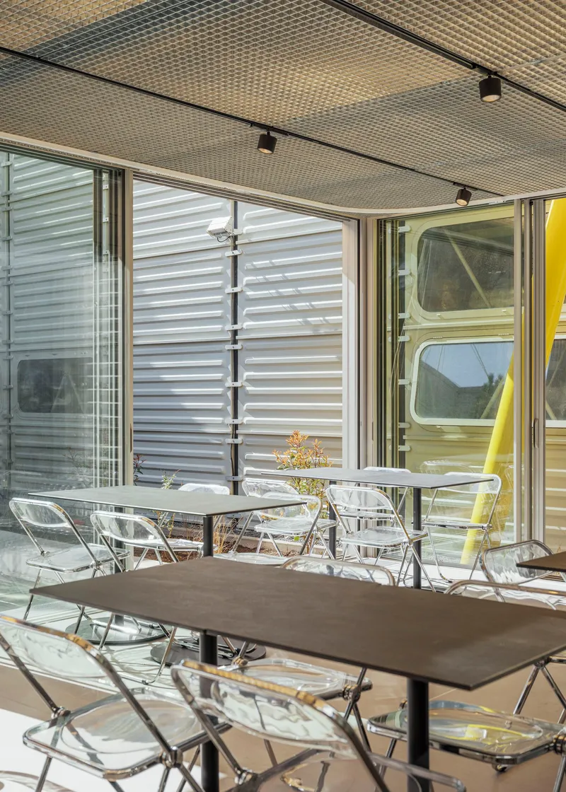 Covered patio with clear acrylic chairs and perforated acoustic ceiling panels beneath retractable awnings