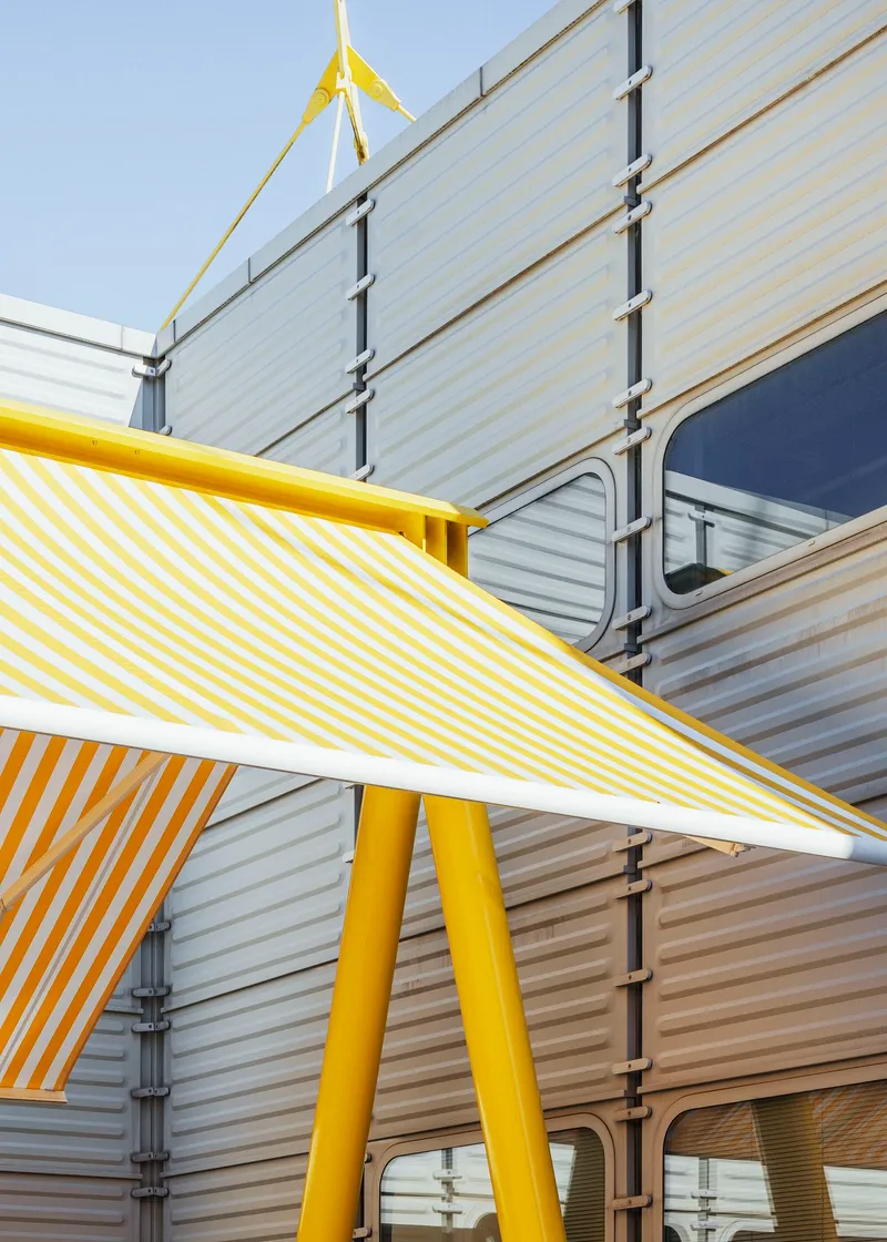 Yellow and white striped canopy blade angled above yellow tubular columns against corrugated wall