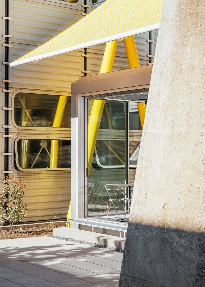 Sliding glass doors beneath yellow canopy with concrete column in foreground casting afternoon shadow