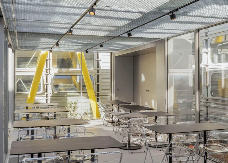 Interior dining area with translucent corrugated ceiling panels, track lighting, and yellow structural columns visible through glazing