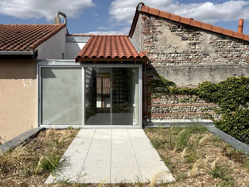 Glass extension with terracotta roof tiles meeting exposed brick wall and gravel courtyard planting