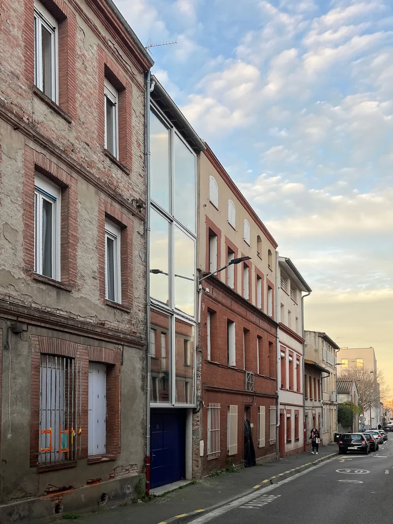 Street elevation showing glass infill facade among brick townhouses at dusk with parked cars