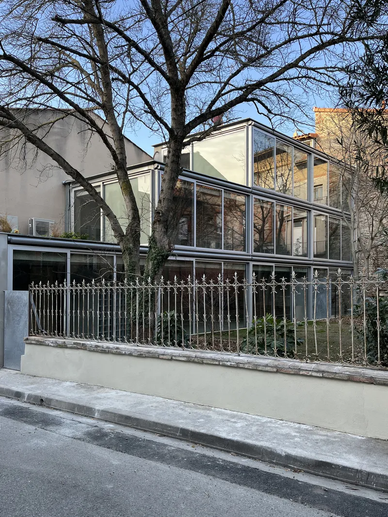 Street view of the white-framed glass extension behind a metal railing and bare winter trees