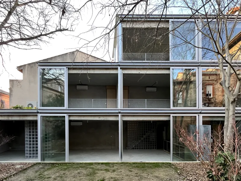 Garden facade showing the stacked white-framed glass bays with perforated metal panels beneath bare branches