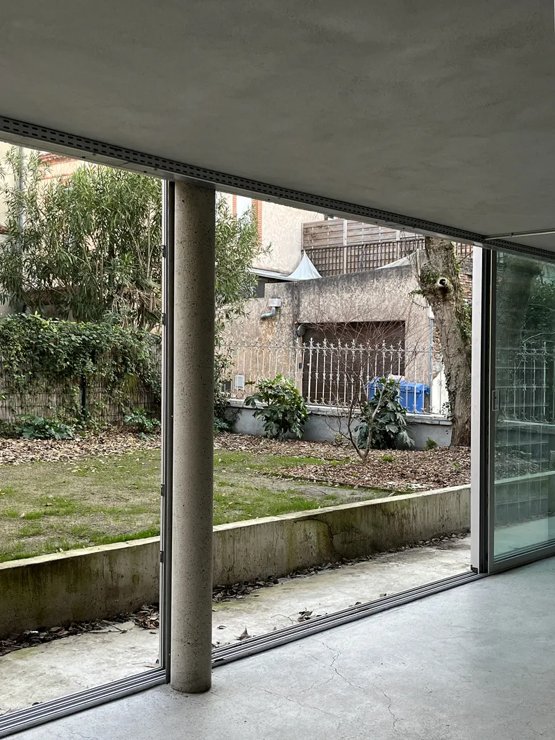 Interior view through floor-to-ceiling glass opening to the garden courtyard with single concrete column