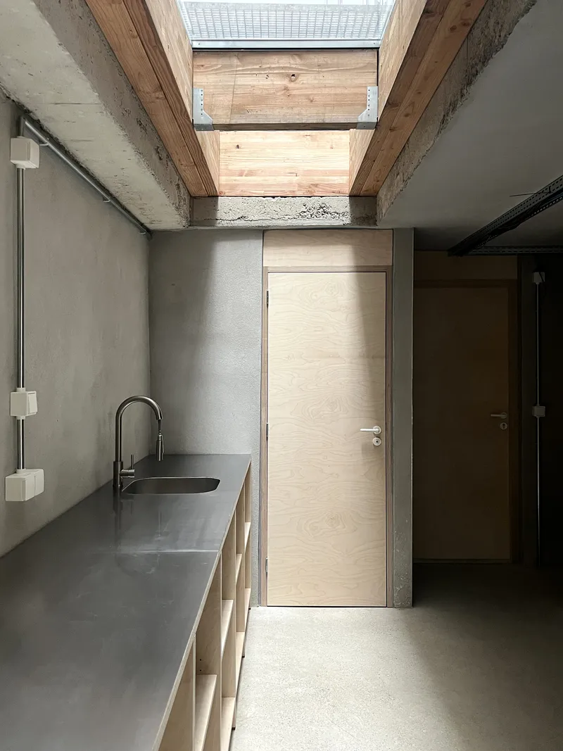 Concrete and timber kitchen corridor with rectangular skylight illuminating the light wood door