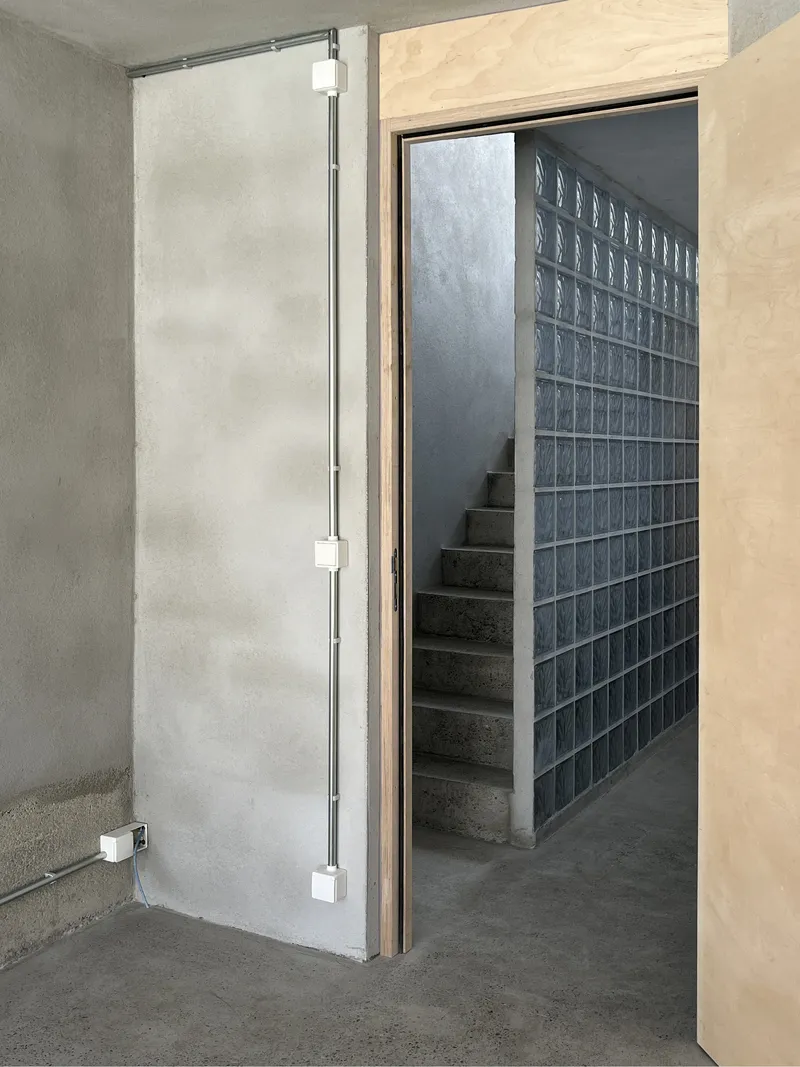 Doorway with light wood frame opening to a concrete stair beside a glass block wall