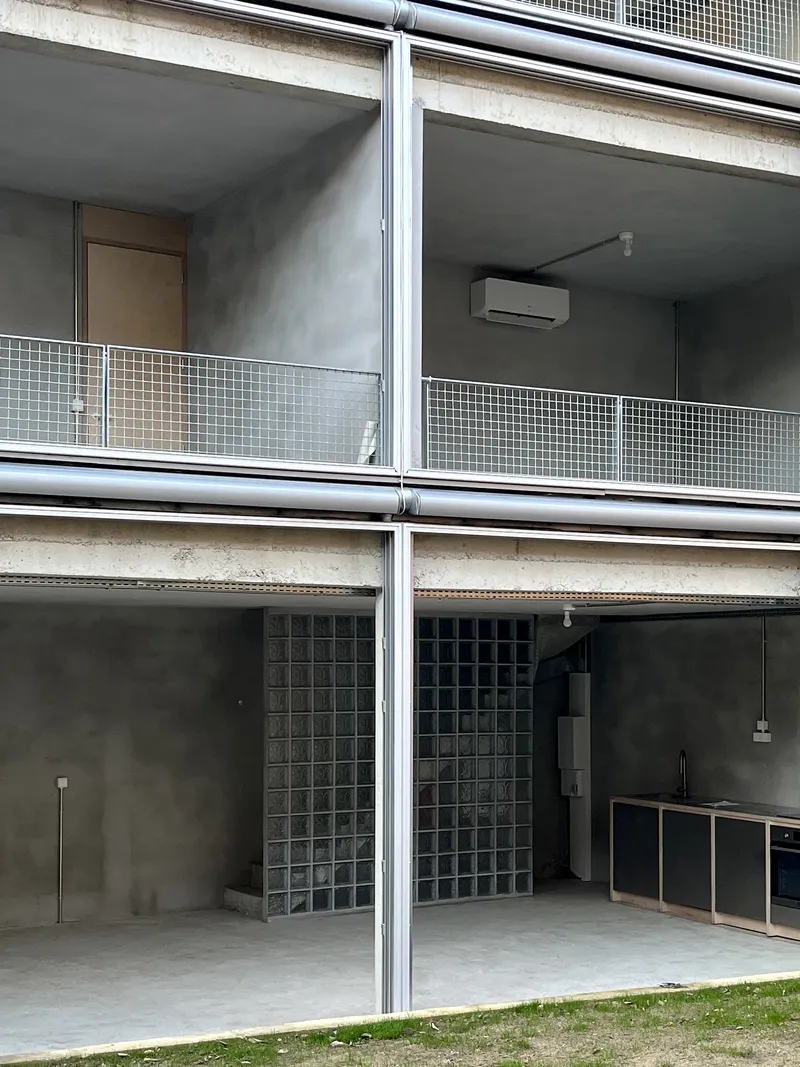 Stacked balconies with glass block walls, metal railings, and concrete soffit under overcast sky