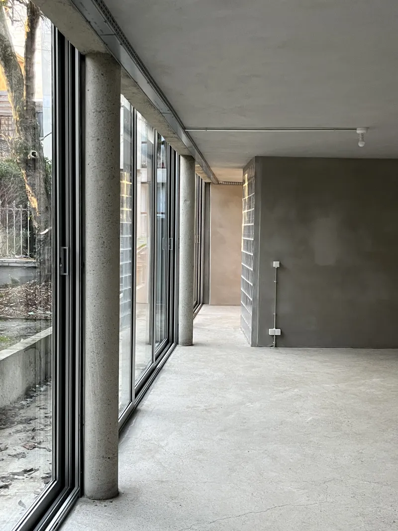 Interior space with floor-to-ceiling glass panels, concrete columns, and polished cement floor in daylight