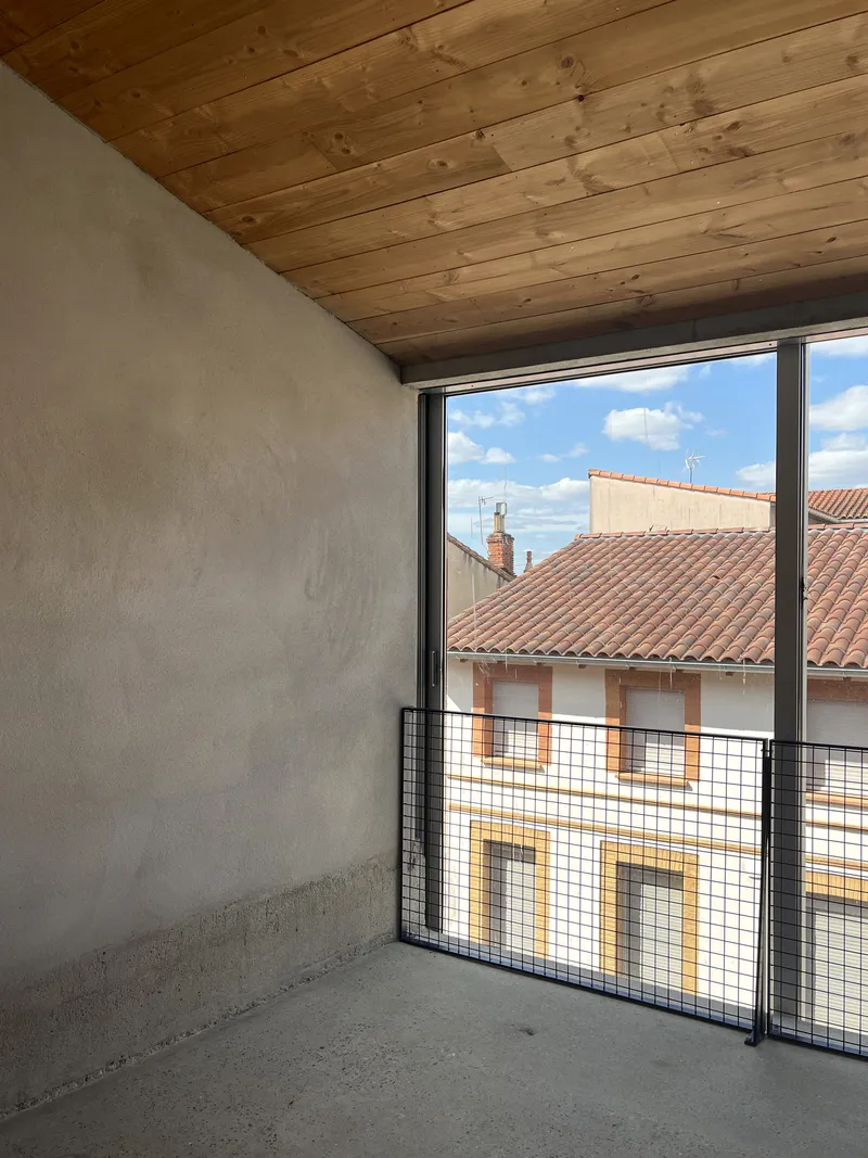 Corner balcony with timber plank ceiling and wire mesh railing overlooking terracotta rooftops under blue sky