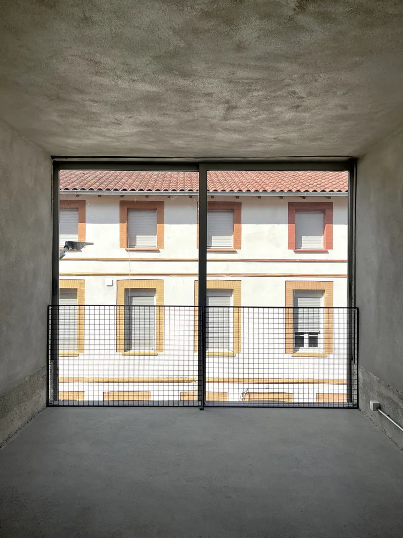 Interior room with concrete walls and floor-to-ceiling glazed doors framing view of neighboring residential facade