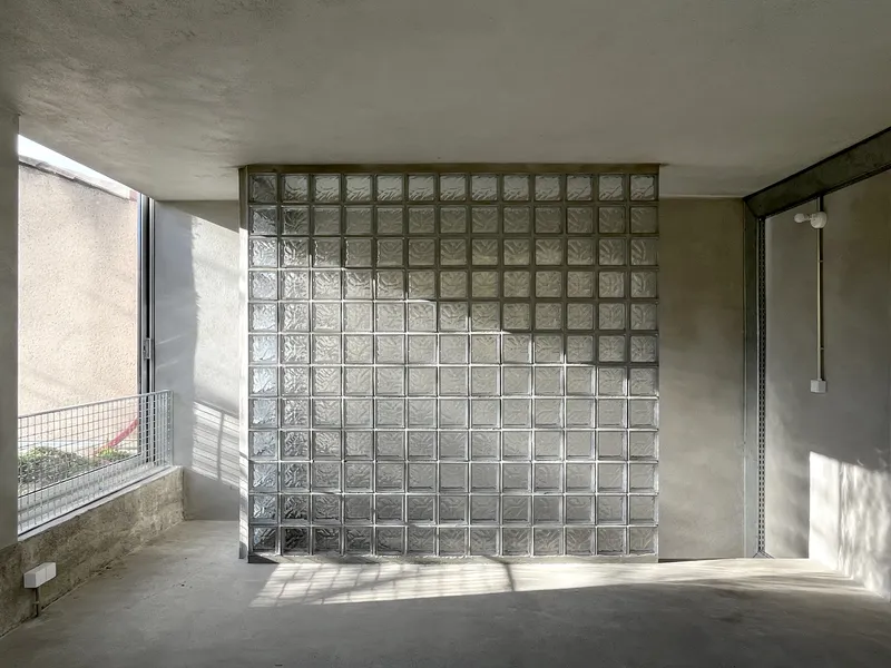 Interior space with freestanding glass block partition wall receiving sharp sunlight from adjacent window opening