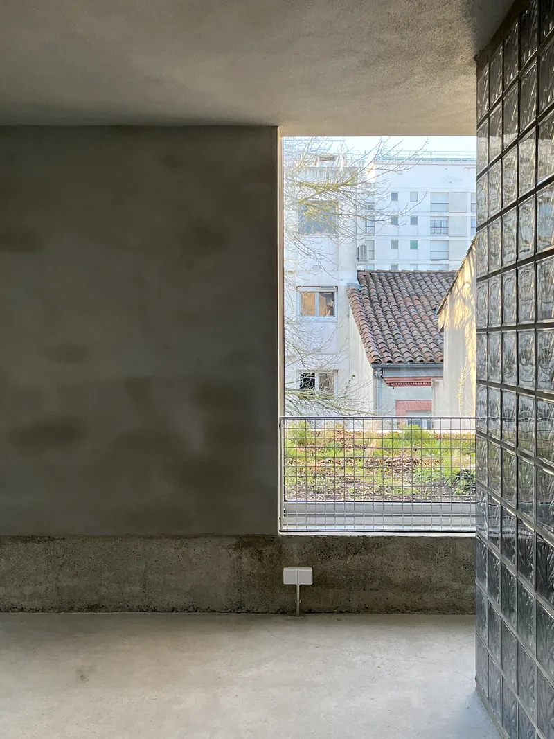 Corner window framed by glass block wall overlooking neighboring buildings and bare winter trees