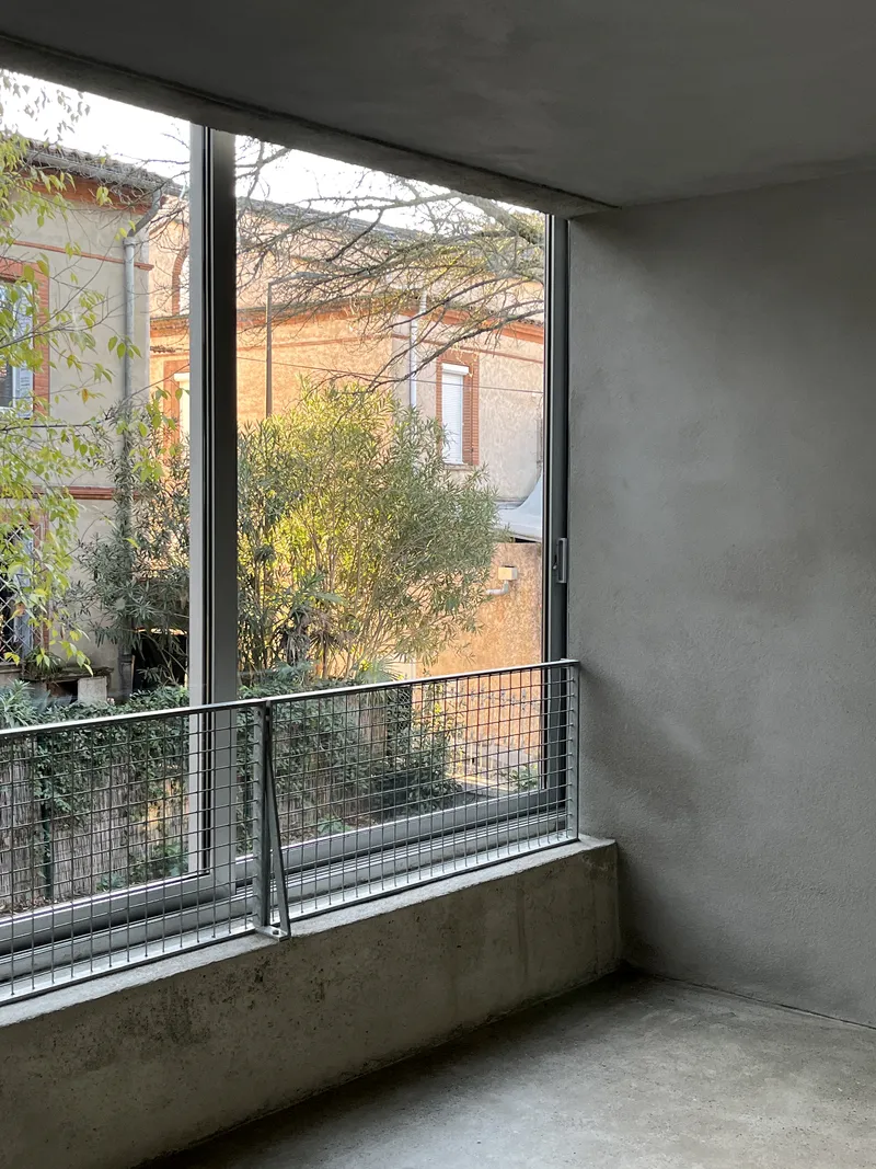 Floor-to-ceiling window with metal railing opening to courtyard garden with leafless branches