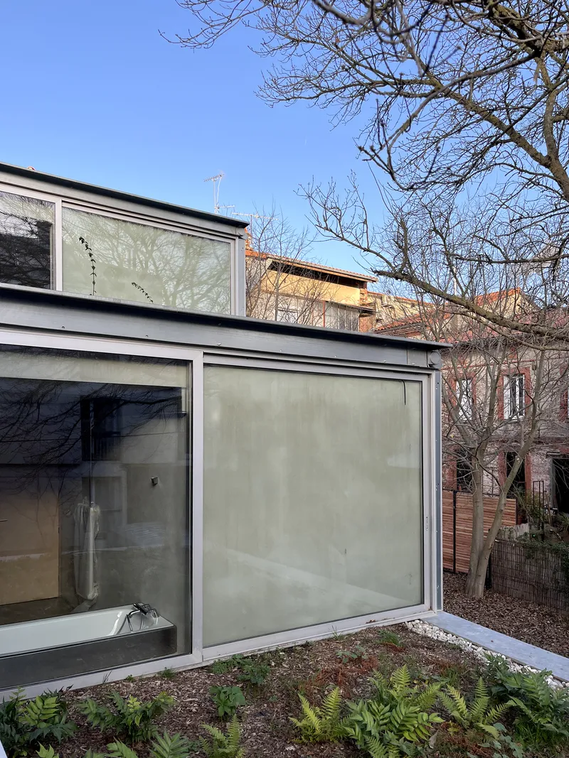 Rear facade with translucent glass panels and metal-framed windows facing planted garden bed
