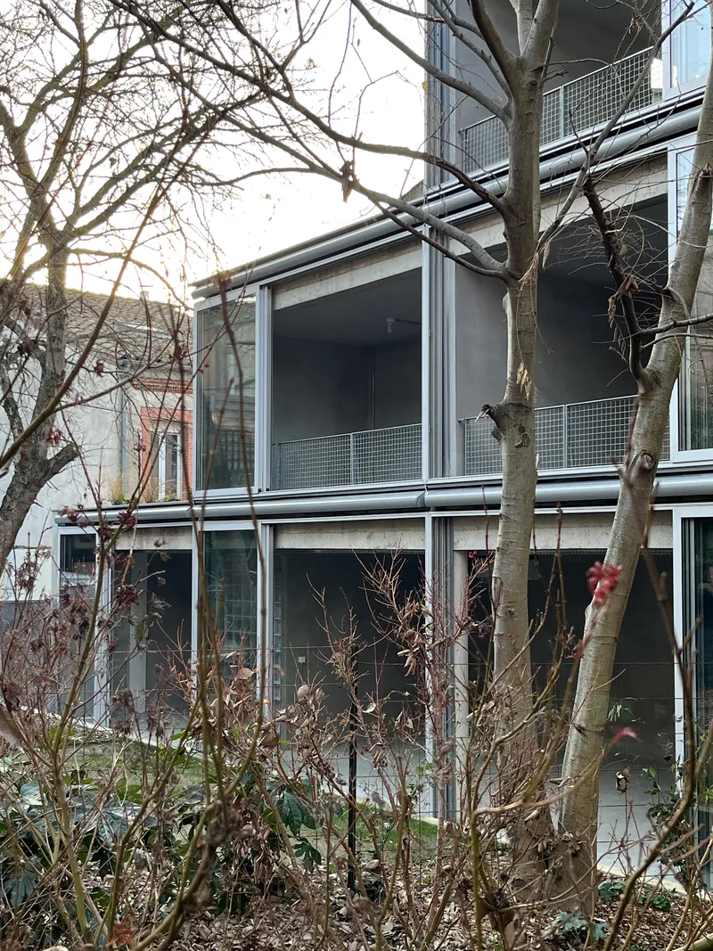 Stacked glazed facade with horizontal metal frames behind bare trees and winter shrubs