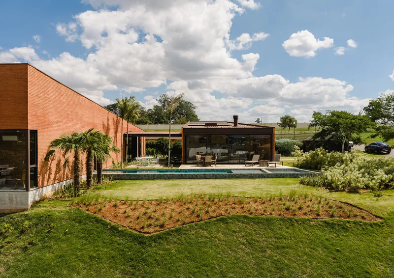 Garden view showing the red brick wing, glazed pavilion and pool terrace under a cloudy sky