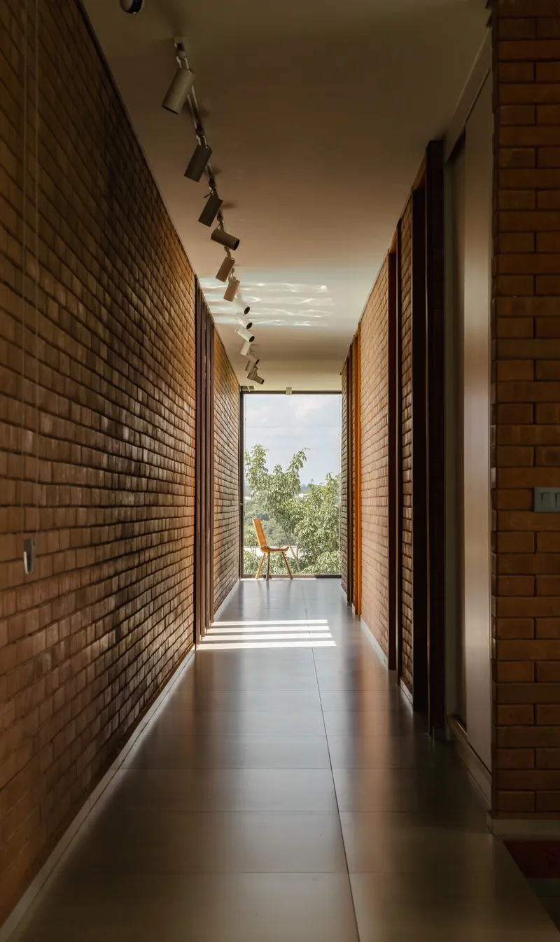 Corridor with brick walls, track lighting and louvered screens filtering daylight from the garden