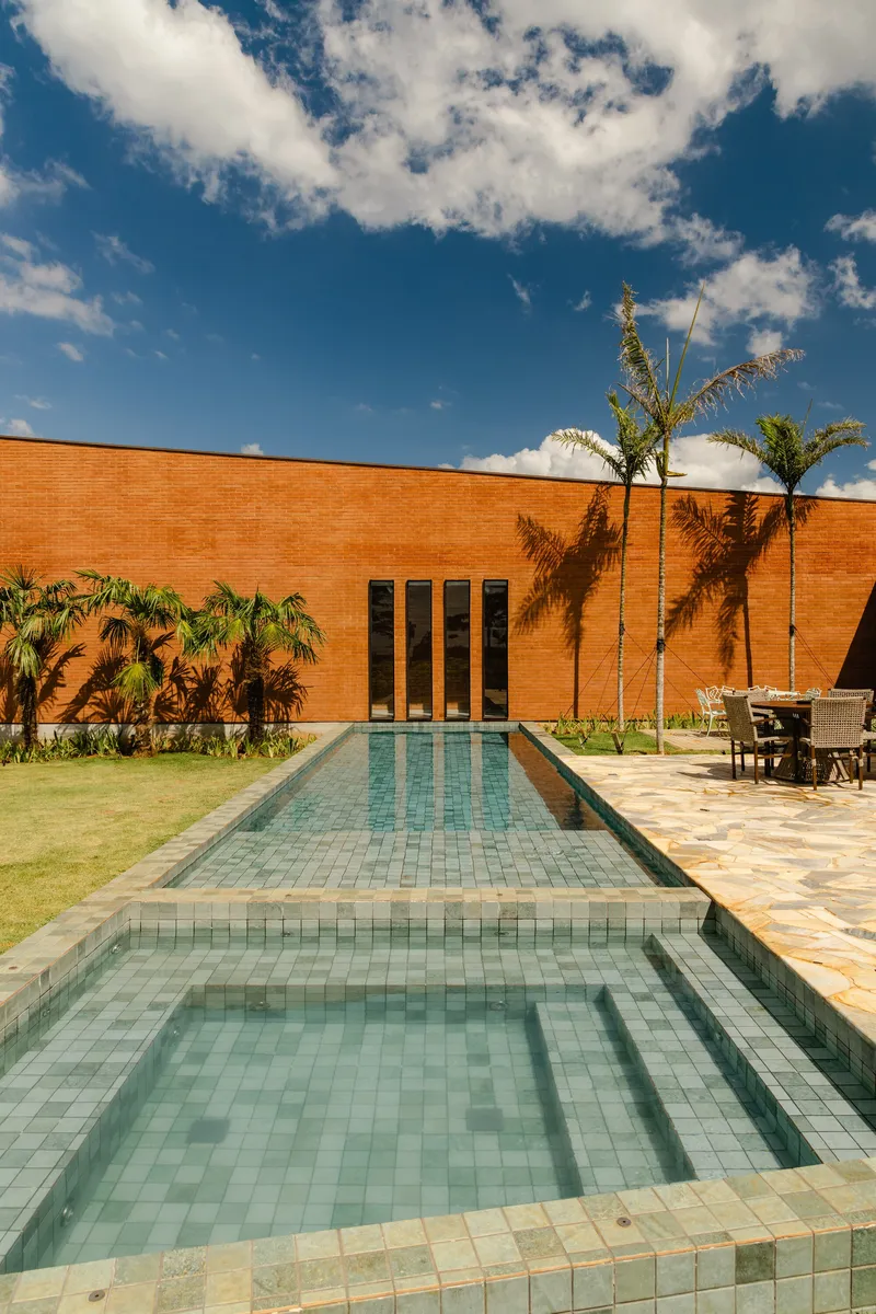 Tiled pool with raised spa flanked by palm trees against the brick courtyard wall